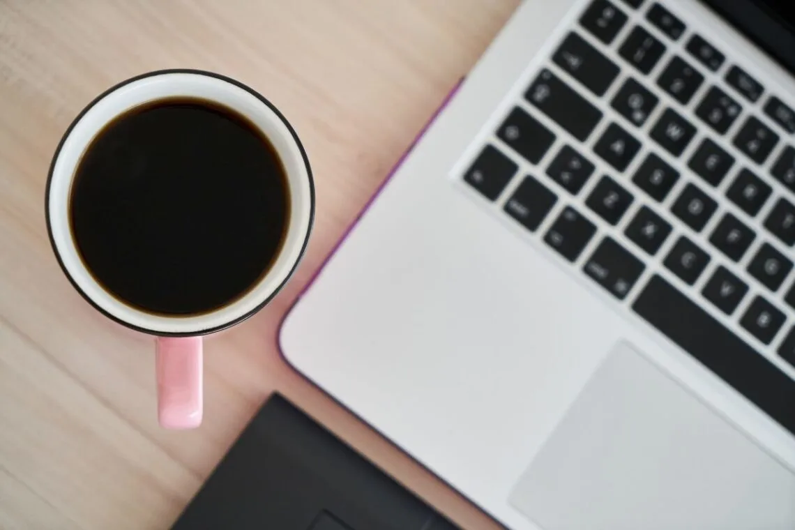 cup of coffee next to an open MacBook
