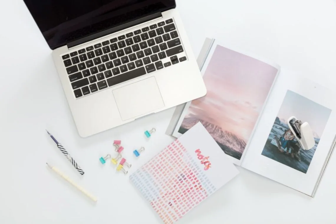 open MacBook on a desk with notebooks and magazines